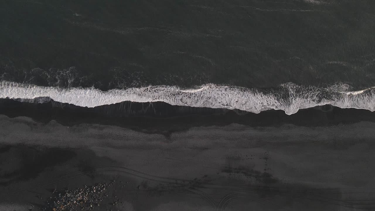 вертикальный вид с воздуха на волны, разбивающиеся о черный песчаный пляж в исландии