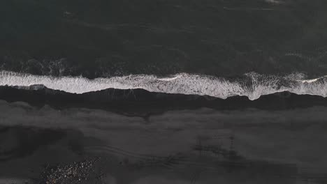 aerial vertical view of waves breaking on black sandy beach in iceland