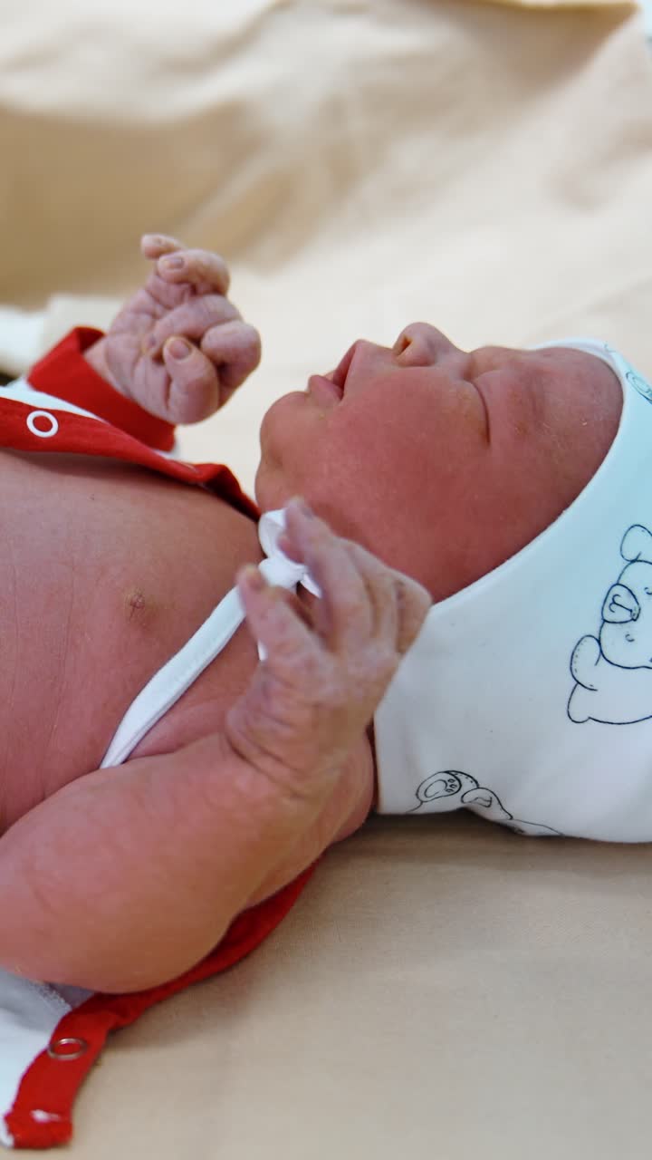 Crying newborn id dressed by the gloved hands of medic. Little child on the doctor's table. Close up. Vertical video