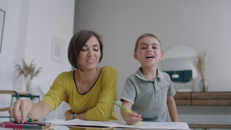 Mother-in-yellow-jacket-and-son-in-t-shirt-sit-at-the-table-and-draw-together-color-pencils-on-paper.-Happy-childhood.-Loving-helps-his-son-in-pre-school-training-and-develops-creativity-in-the-child