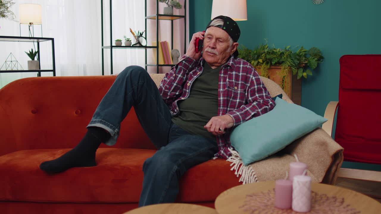 счастливый стильный пожилой дедушка мужчина с смартфоном разговаривает с друзьями дома, разговор