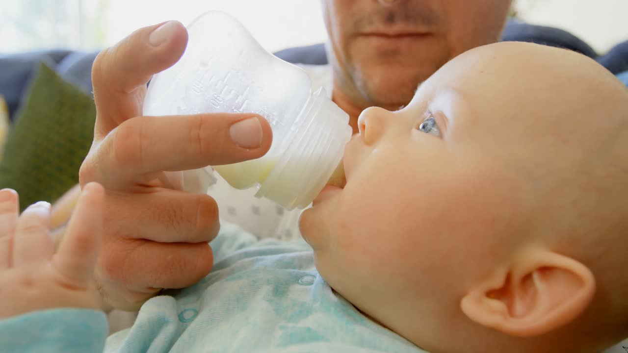 Padre che dà il latte al suo bambino in salotto 4k