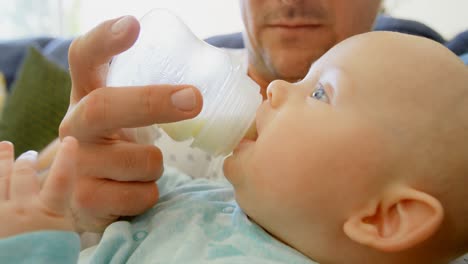 padre alimentando leche a su bebé en la sala de estar 4k