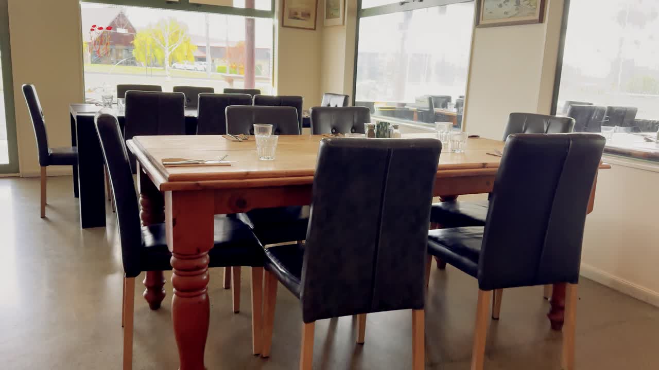 Daytime camera pan across a modern, empty cafe in Lake Tekapo, highlighting wooden tables, black chairs, natural light, and clean dining setup