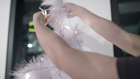 a person wrapping white blinking christmas lights around a small white christmas tree while decorating for the holidays