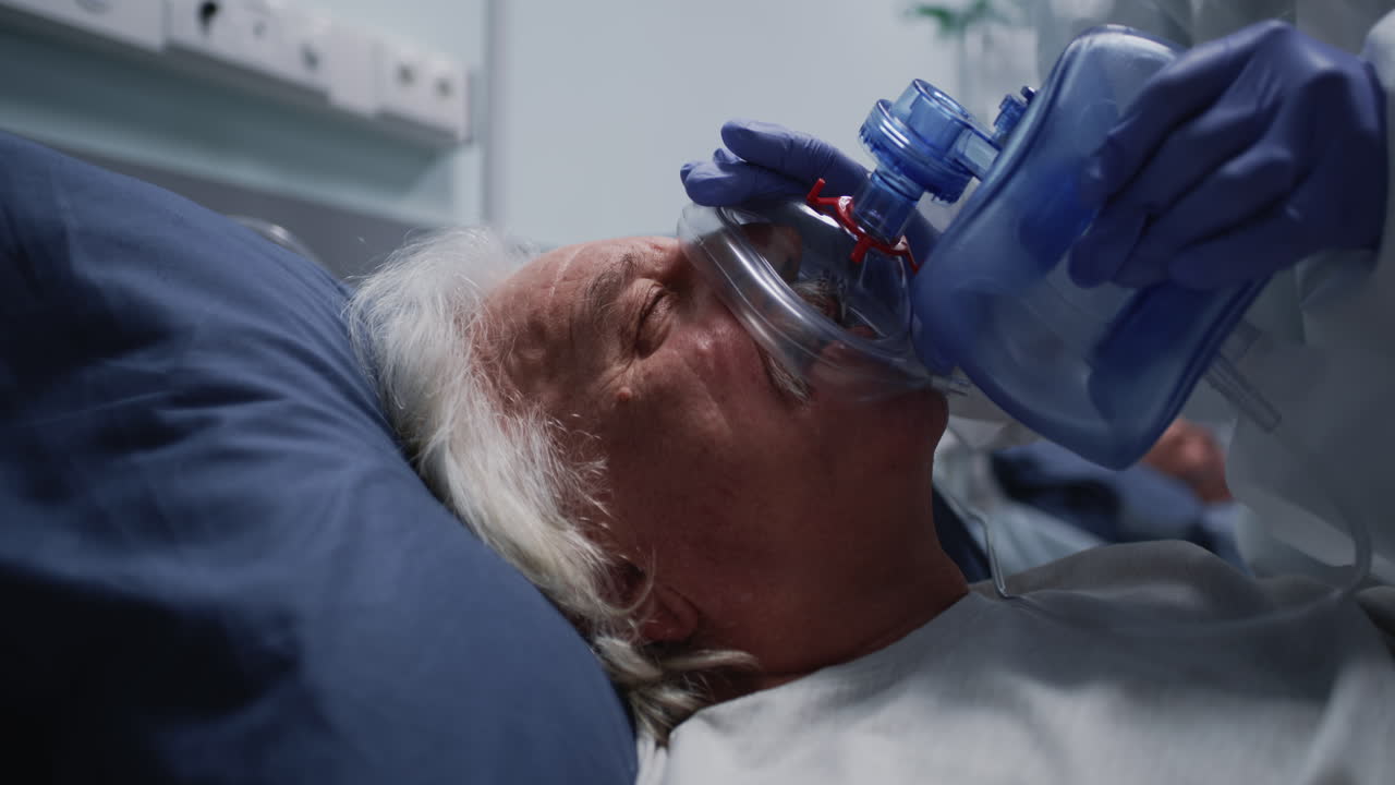 Medical professional in PPE administers oxygen to an elderly patient in a hospital intensive care unit