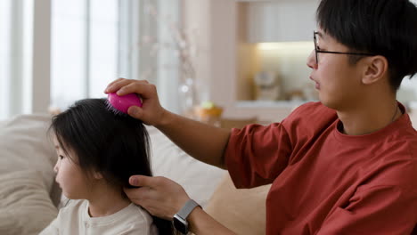 Father combing daughter's hair at home