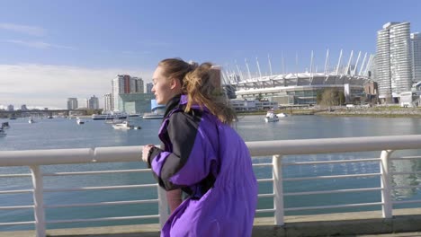 athletic young woman running in city across bridge wearing jacket