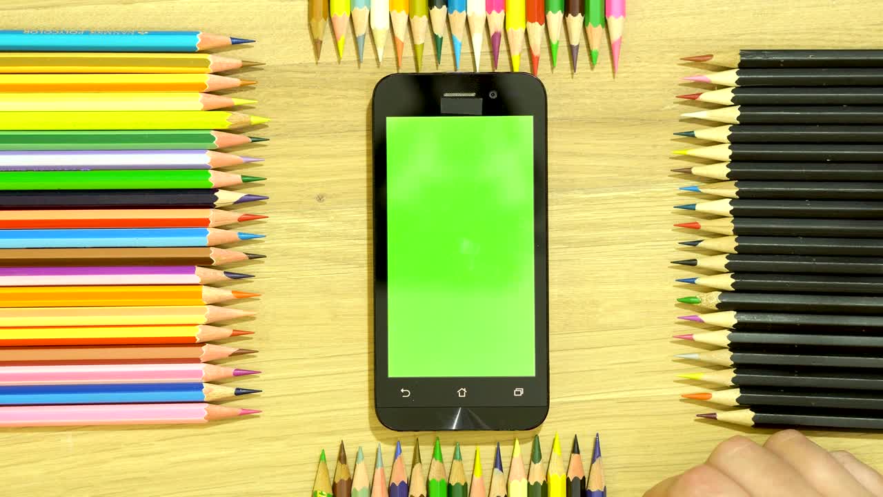 lápices de color en la mesa a lo largo del perímetro. mano en el teléfono inteligente.