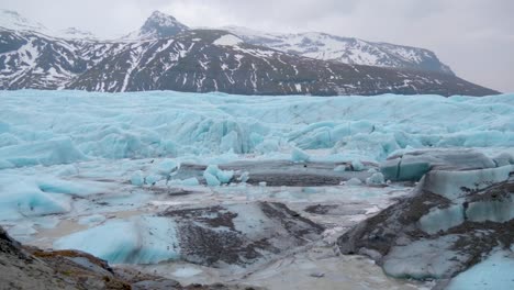estática, toma del mar, en el glaciar turquesa skaftafellsjokull, montañas nevadas en el fondo, en un día nublado, en la costa sur de islandia