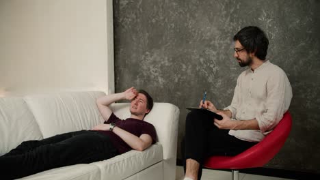 displeased man talking about his issues at therapy session with counselor, lying on sofa