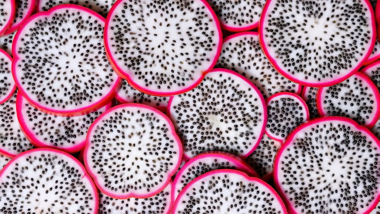 Skåret pitaya i flatlay-mønster som viser frem levende magentarosa skall og flekket hvitt fruktkjøtt i et tett, repeterende mønster.