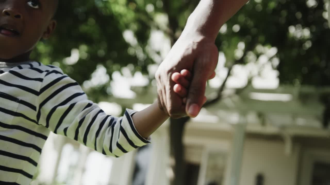 tomando de las manos de un hijo y un padre afroamericanos caminando en un jardín soleado, cámara lenta