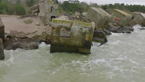 Vista-Aérea-De-Establecimiento-De-Edificios-De-Fortificación-Costeros-Abandonados-En-Los-Fuertes-Del-Norte-De-Karosta,-Costa-Del-Mar-Báltico,-Grandes-Olas,-Día-Nublado,-Cámara-Lenta,-Disparo-De-Drones-Moviéndose-Hacia-Atrás