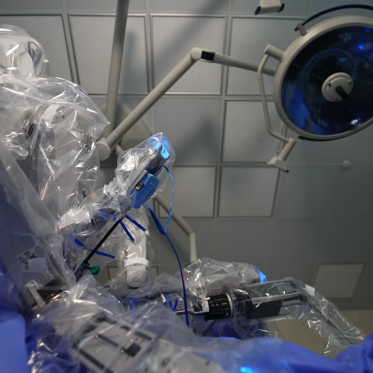 Da Vinci surgery system operating the patient. Manipulator arms coated with plastic move slowly back and forth. Low angle view