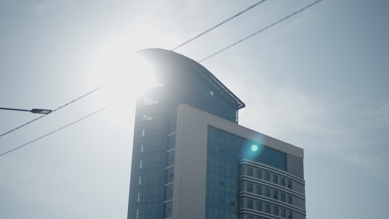 Modern glass tower with sun bursting behind roof, minimalist sky, power wires crossing frame, urban skyline mood, corporate architecture exterior, high rise office landmark under clear daylight