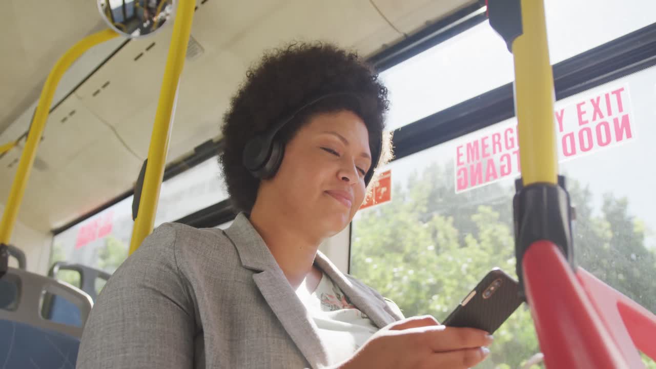 mujer biracial feliz de talla plus usando un teléfono inteligente en el autobús