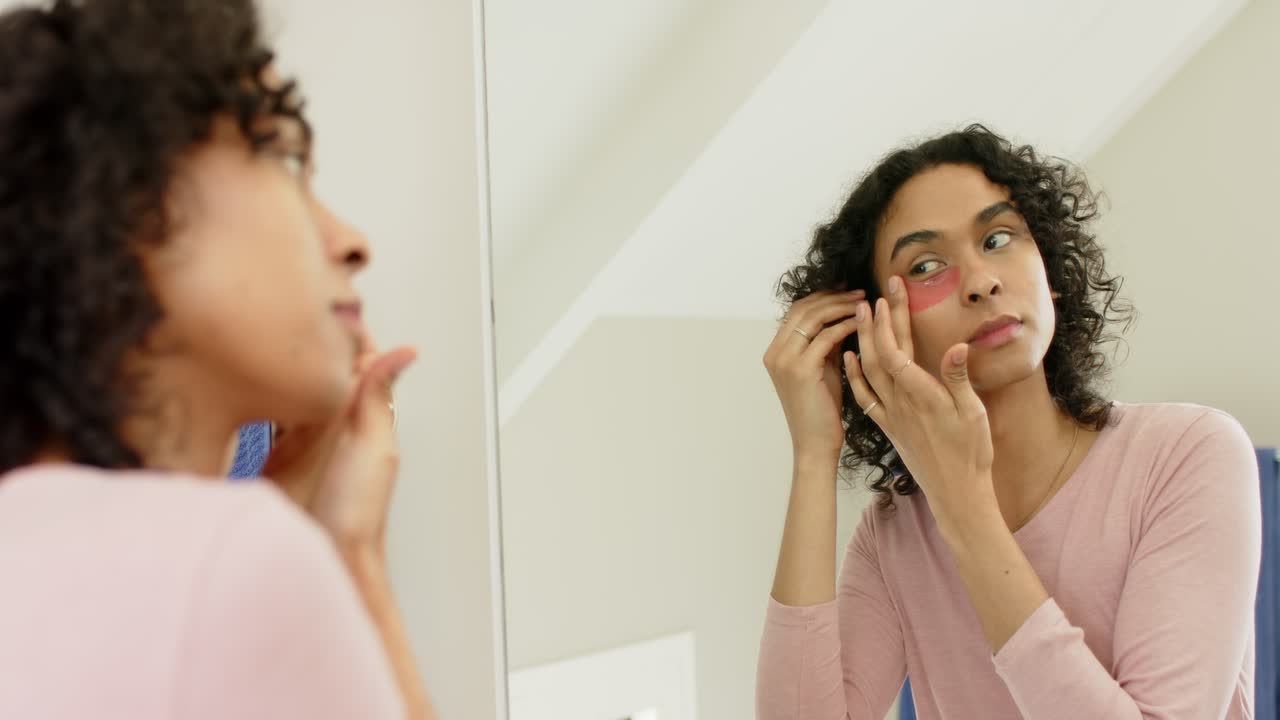 Non-binary person grabbing sponge, dabbing blush before placing gel patch in bathroom for skincare