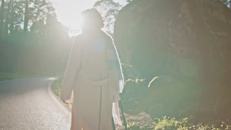 silhouette woman walking forest road at dawn backlit by morning sunlight.