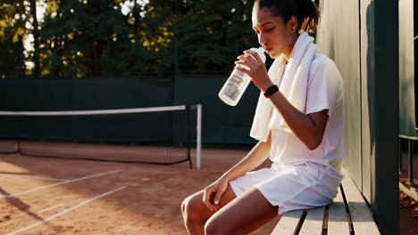 female tennis player resting on court with a water bottle