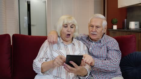 Pareja-De-Jubilados-Mayores-Con-Tableta-Digital-En-Casa.-Descansando-En-El-Sofá-En-La-Acogedora-Sala-De-Estar