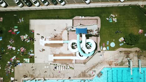 lowering drone shot directly above a large - twisty double waterslide at an outdoor public pool