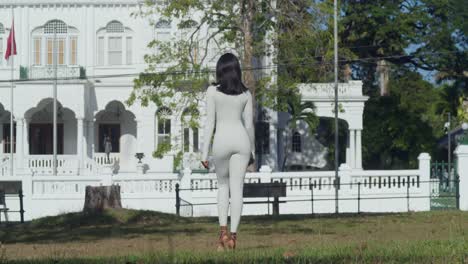 Una-Joven-Vestida-Con-Un-Traje-Blanco-Es-Capturada-En-Una-Ciudad-Caribeña,-Con-Majestuosos-Castillos-Al-Fondo.