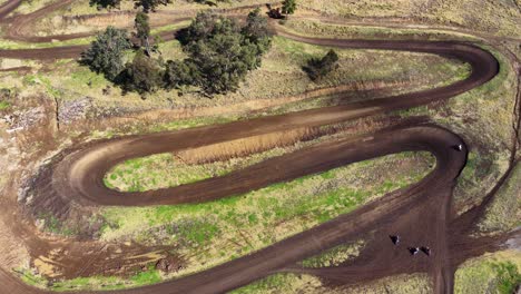 multiple dirt bikes navigate sharp turns on a winding dirt track in rural australia, captured from above with steady daylight drone footage
