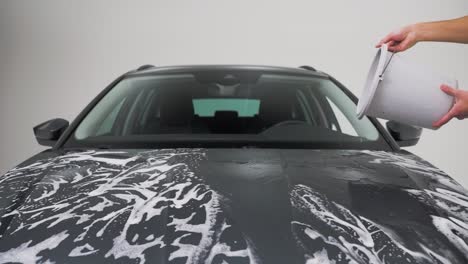 un hombre vertiendo agua sobre un coche jabonado