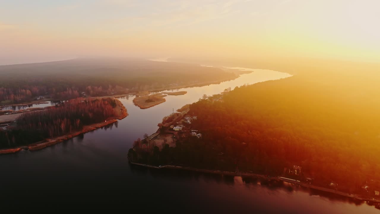 Aerial view of Buļļupe flowing into Lielupe at sunrise with warm misty glow