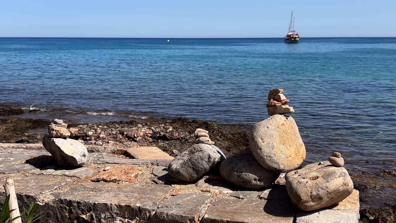Stacked rocks on the coastline of Crete Greece with turquoise sea and a boat in the distance