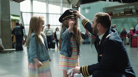 joyful littke girls trying put on dadies pilot cap in airport terminal, looking happy and laughing. cinematic shot on red camera.