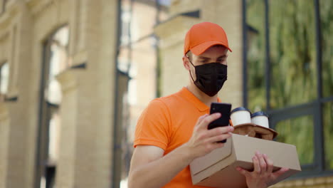 mask courier using smartphone outside. delivery man carrying order outdoors.