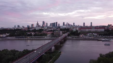 drone footage of warsaw skyline and vistula river with a bridge on a magical pink sunset with cinematic roll back