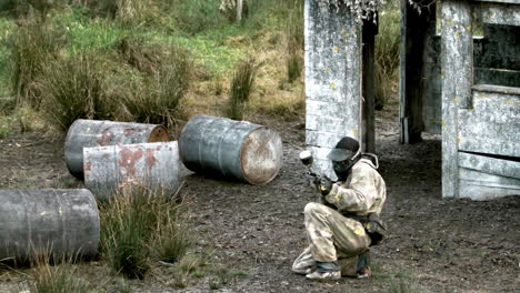 man crouching on ground and getting shot at paintball