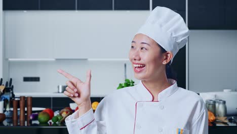 close up of asian woman chef smiling and pointing to side in home kitchen