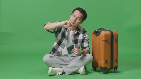 full body of asian male traveler with luggage and passport looking at camera and showing thumbs down gesture in the green screen background studio