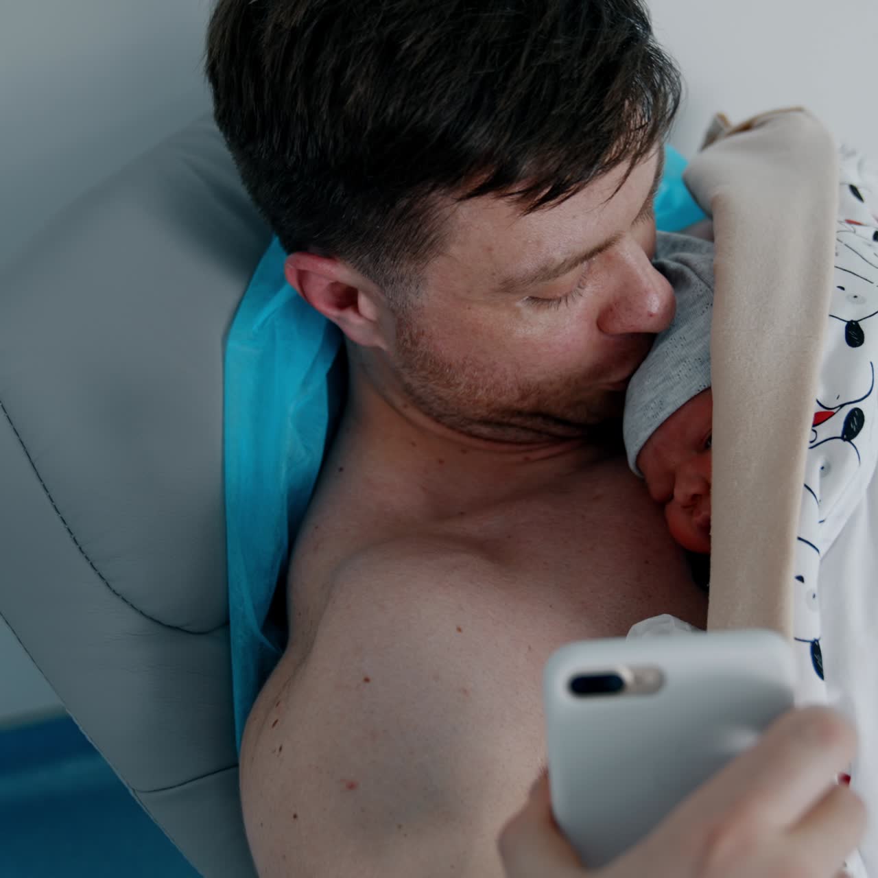Caucasian father is taking video on the phone. Happy dad showing his newborn baby lying on his chest. Top view