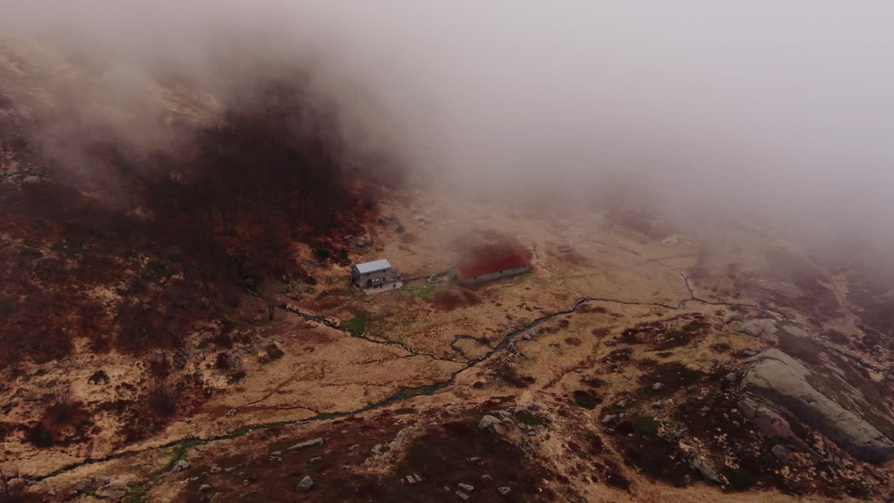 Mist-covered landscape in the Dolomites Mountains, showcasing a remote cabin and winding paths