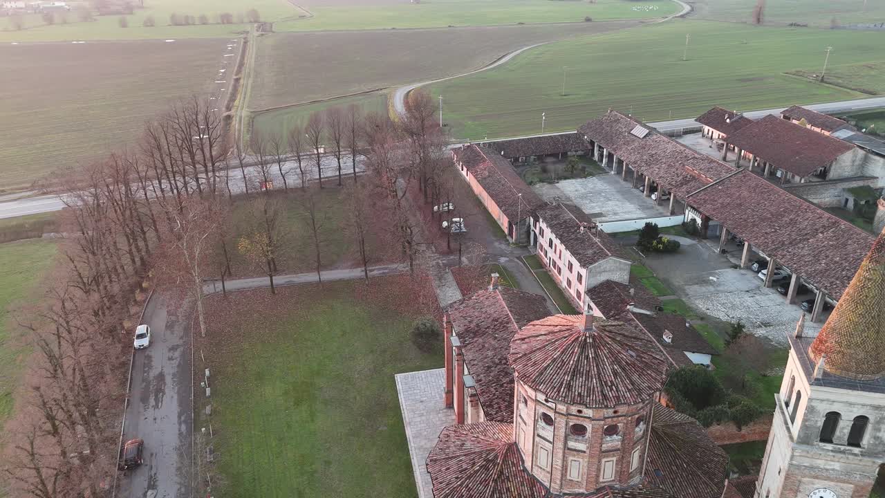 Vista aérea do Santuário da Bem-Aventurada Virgem da Misericórdia ao lado da Strada Paullese Strada Provinciale SP 415 para o contorno de Milano, estrada moderna através dos campos rurais da Lombardia ao pôr do sol