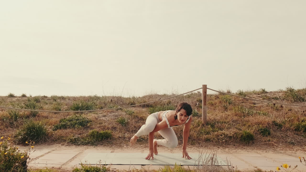 Mujer joven practicando una postura de equilibrio de brazos de yoga al aire libre.