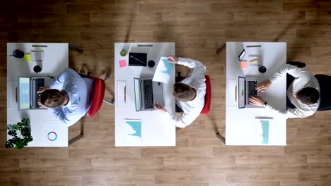 three young businessman are working on laptops, pass diagrams, work concept, office concept, communication concept, top shot