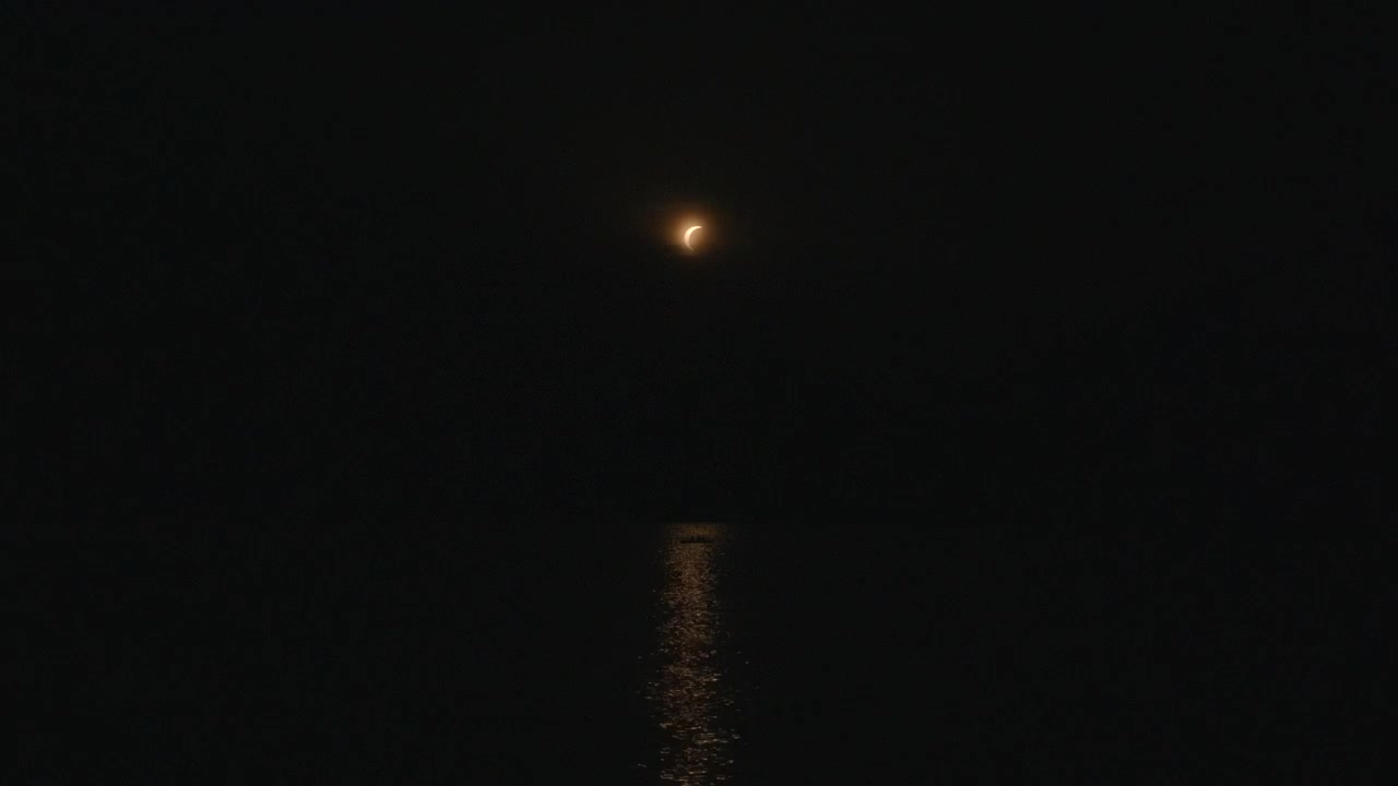 Una piccola luna crescente luminosa pende sopra un mare scuro e calmo, con dettagli di luna, falce di luna, notte e paesaggio marino, che mostrano oceano, acqua, riflesso, un contesto scuro, con dettagli chiaramente visibili, per uso commerciale