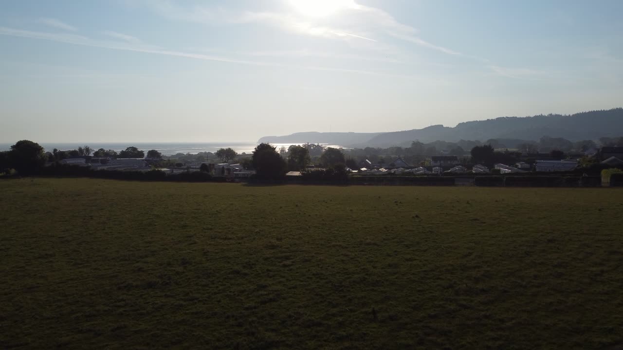 해가 뜨는 웨일스 카라반 파크 에서 빛나는 해안 만 과 굴러다니는 시골 언덕 을 내려다보며 천천히 상승 하고 있다