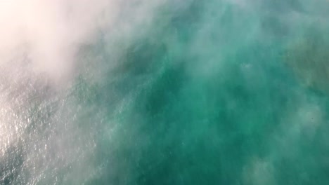 aerial: beautiful blue ocean can be seen through the fog as we tilt up to reveal an oregon coastline mountain