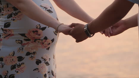 hands of a young couple a man holds his pregnant wife only belly and hands are visible in the frame