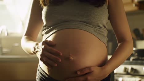 a woman gently cradles her baby bump while standing in a warm and inviting kitchen. soft light filters through the window, creating a serene atmosphere as she prepares for motherhood.