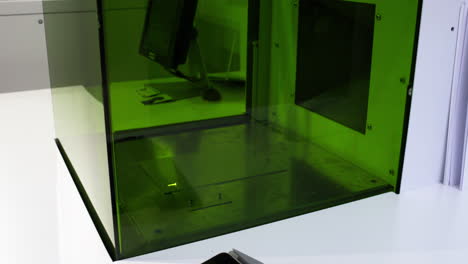 laser engraving a design into a metal plate behind green safety glass