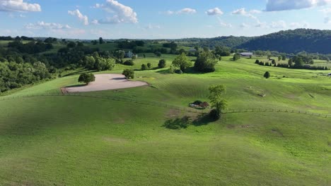 Verde-Brillante-Y-Exuberante-Tierra-De-Pastos-De-Kentucky-Con-Un-Cielo-Azul-Brillante-Moviéndose-Hacia-Una-Casa-De-Estilo-Sureño-En-Una-Plataforma-Aérea-De-Colina