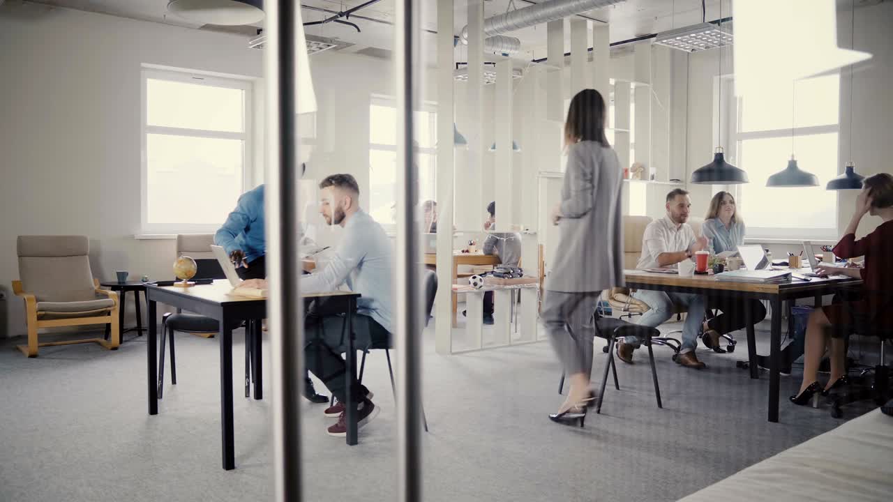 Dolly shot of happy mixed ethnicity office colleagues enjoying working at healthy office. View through glass wall 4K